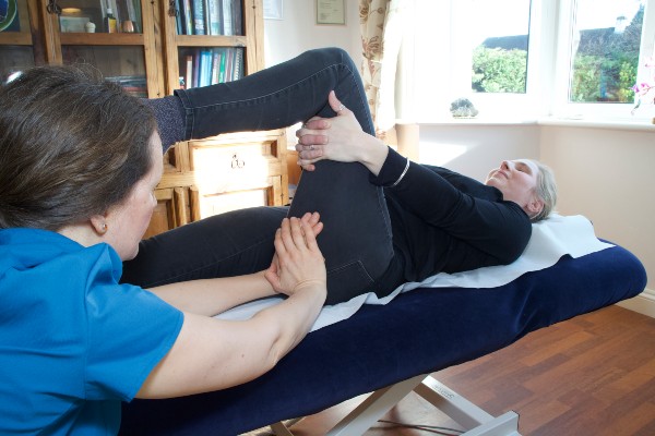 Chiropractor places leg on client's thigh to perform an adjustment.